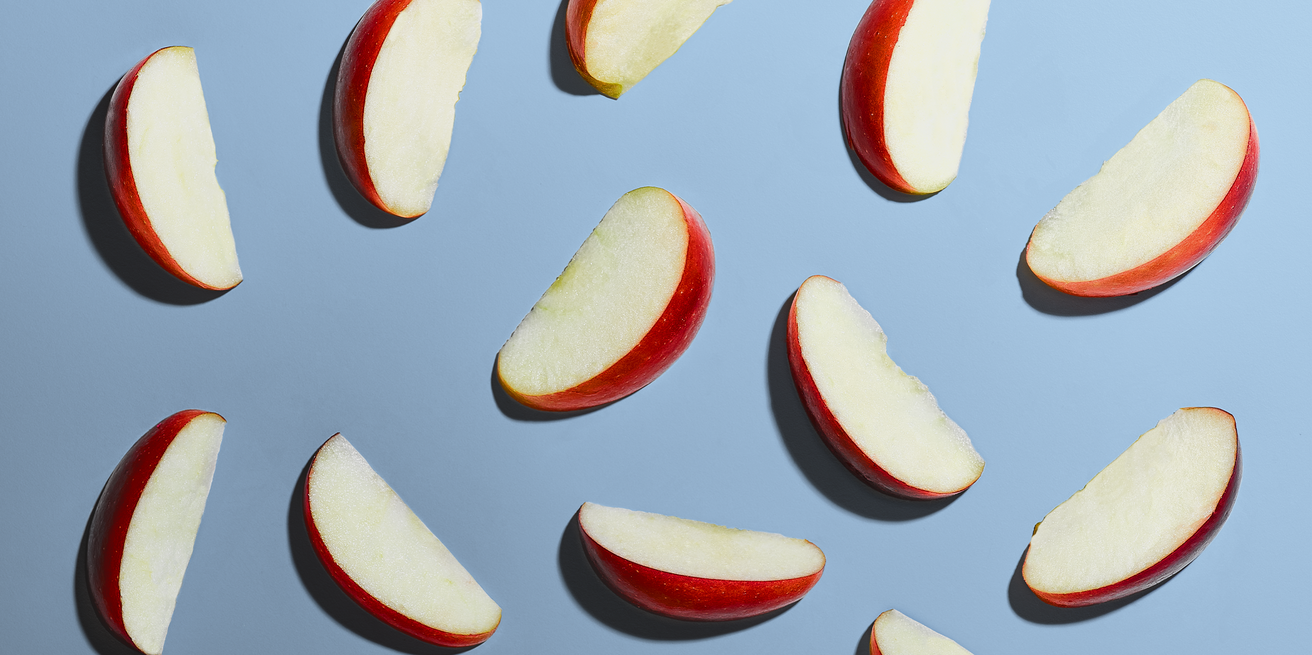 12 individual apple slices laid flat on a blue background.