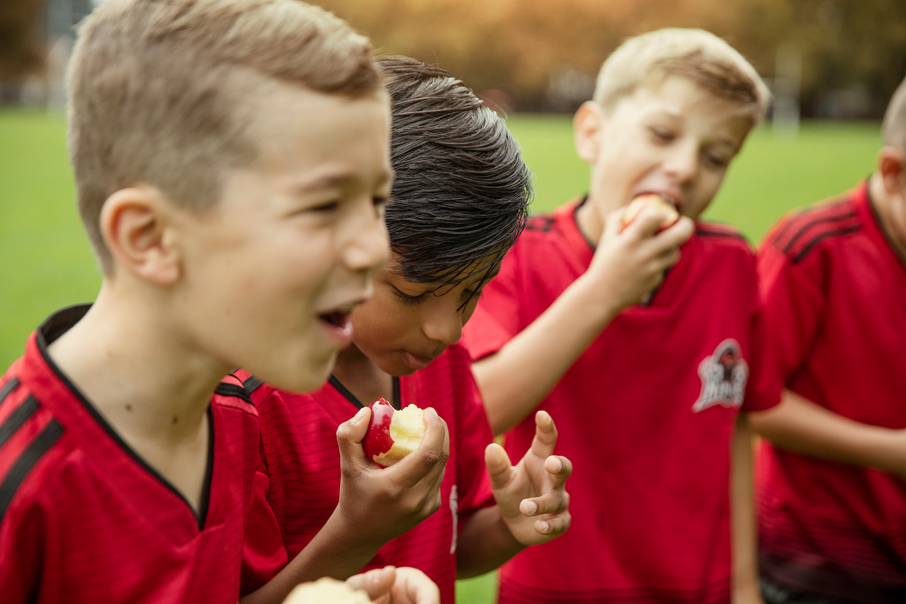 four kids eating apples after football match